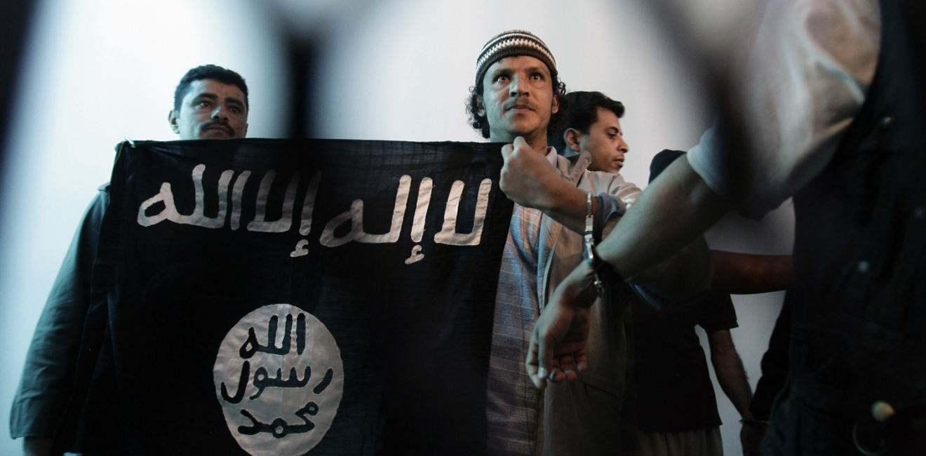 n this April 23, 2013 file photo, a suspected Yemeni al-Qaida militant, center, holds a banner as he stands behind bars during a court hearing in state security court in Sanaa, Yemen