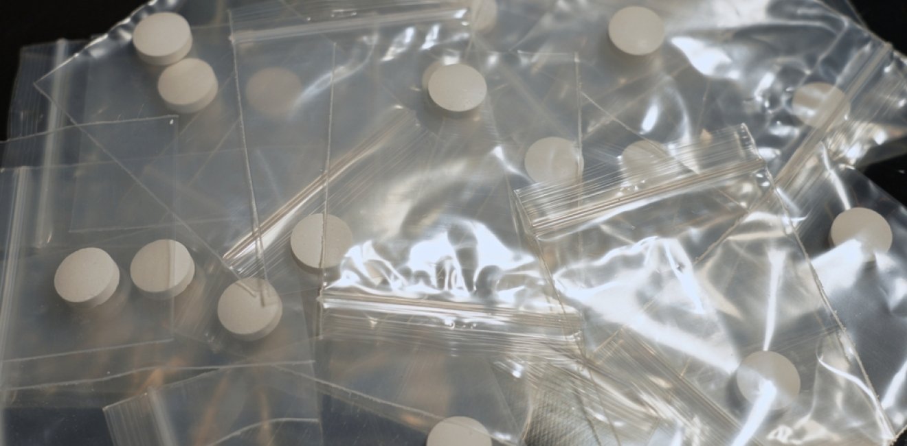 Table of drug dealer with fentanyl pills in pressed powder packed in small bag, heroin and methamphetamines, illicit drugs. Dangerous fentanyl and money bill evidence at a crime scene.