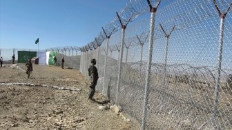 A uniformed soldier stands at a wire border fence.