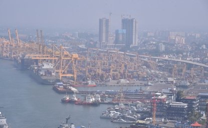 An aerial view of a port with cranes, ships, and skyscrapers.