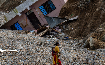 A woman with a child on her back walks past a house which had collapsed due to flooding in the Nakhu river caused by heavy rains in Lalitpur, Nepal, on Tuesday, October 1, 2024. AP Photo/Niranjan Shrestha.