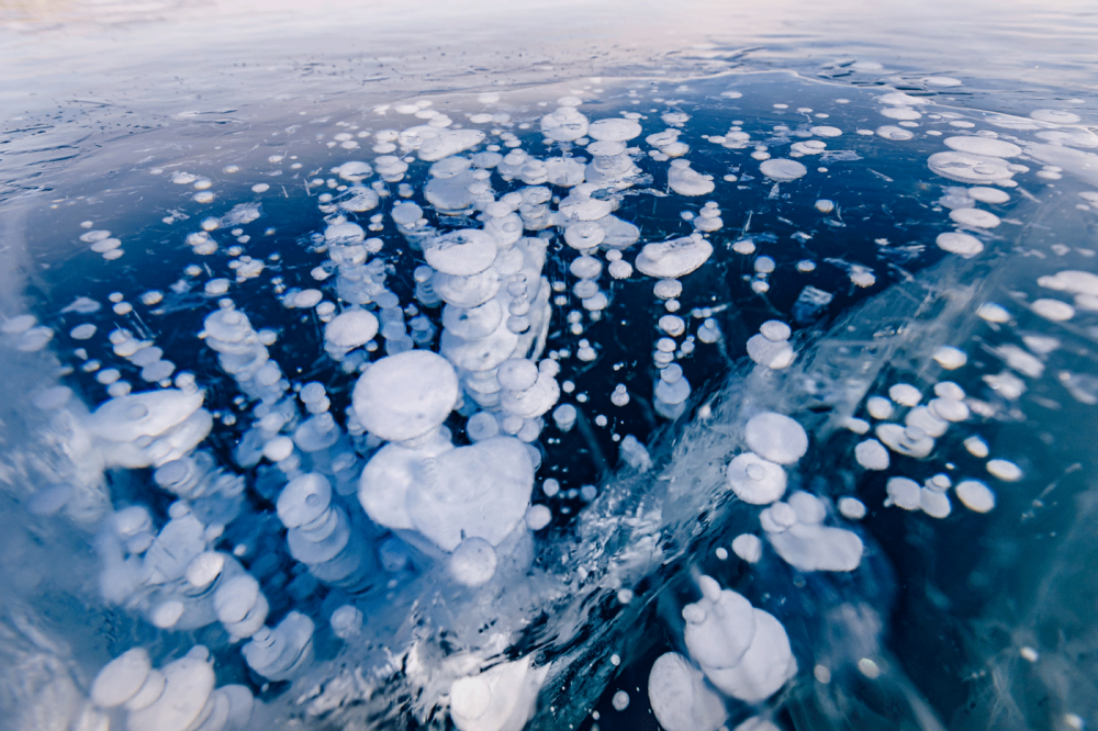 Gas methane bubbles frozen in winter ice of lake Baikal, abstract background.