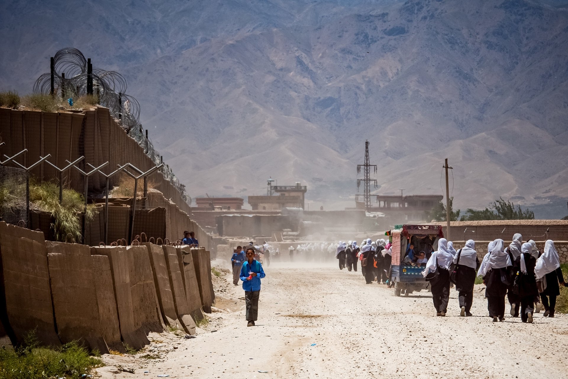 People walking down a dirt road in between buildings.