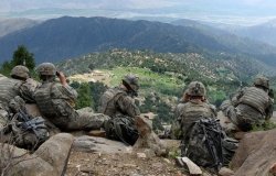 Five U.S. soldiers sit on a ridge looking out at a valley in Afghanistan.