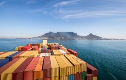 Large stacked container ship leaving the port of Cape Town with Table mountain and the city in the background, South Africa.